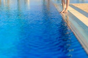 jovem mulher pernas em pé em fronteira frente do natação piscina foto