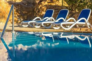 espreguiçadeiras perto natação piscina e refletido seus dentro azul água foto