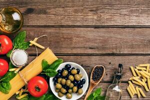 cru ingredientes para a preparação do italiano massa, espaguete, manjericão, tomates, azeitonas e Oliva óleo em de madeira fundo. topo visualizar. cópia de espaço. foto