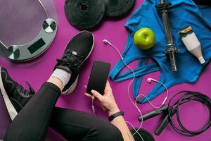 jovem mulher com Móvel telefone e esporte equipamento em cor fundo plano deitar topo visualizar. ginástica conceito foto