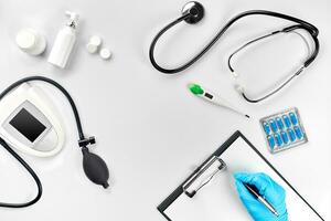 local de trabalho do uma doutor. pílulas dentro mão, estetoscópio, prancheta e óculos em branco mesa foto