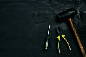 chaves de fenda, martelo, alicate e Ferramentas em uma Preto de madeira mesa. topo Visão foto