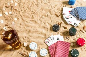 poker de praia. salgadinhos e cartões em a areia. por aí a conchas do mar e frio beber dentro uma vidro. topo Visão foto