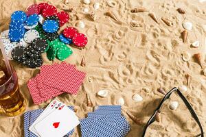 poker de praia. salgadinhos e cartões em a areia. por aí a conchas, oculos de sol e frio beber dentro uma vidro. topo Visão foto