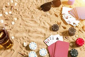 poker de praia. salgadinhos e cartões em a areia. por aí a conchas, oculos de sol e frio beber dentro uma vidro. topo Visão foto