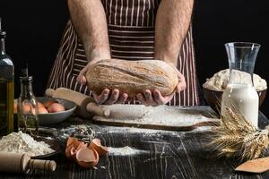 chefe de cozinha detém a fresco pão dentro mão. homem preparando massa às mesa dentro cozinha. foto