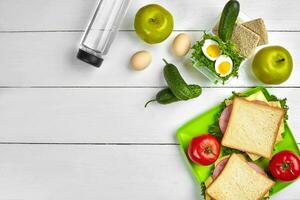 almoço. verde prato com sanduíches e fresco vegetais, garrafa do água e verde maçã em de madeira mesa. saudável comendo conceito. topo Visão foto