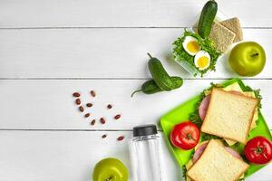 almoço. sanduíche e fresco vegetais, garrafa do água, nozes e frutas em branco de madeira fundo. saudável comendo conceito. topo Visão com cópia de espaço foto