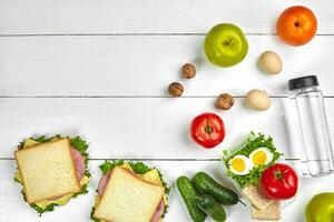 almoço. sanduíche e fresco vegetais, garrafa do água, nozes e frutas em branco de madeira fundo. saudável comendo conceito. topo Visão com cópia de espaço foto