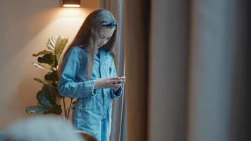 garota em pé digitando em um smartphone em frente à janela foto
