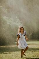 garotinha fofa se divertindo sob o aspersor de irrigação foto