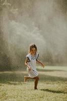 garotinha fofa se divertindo sob o aspersor de irrigação foto