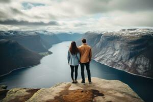 casal em pé em a Beira do uma penhasco e olhando às a fiorde, traseiro Visão do casal família viajando juntos em penhasco Beira dentro Noruega, ai gerado foto