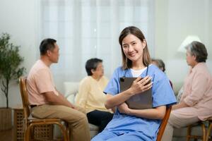 retrato do ásia fêmea enfermeira usando digital tábua dentro enfermagem casa com Senior pessoas em fundo foto