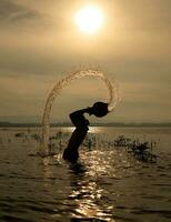 silhueta do uma pescador dentro a água às pôr do sol, tailândia. foto