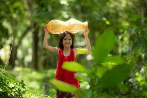 pequeno ásia menina dentro vermelho vestir segurando pescaria equipamento dentro a floresta, rural Tailândia vivo vida conceito foto