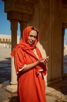 lindo meio Oriental muçulmano mulher com cabeça coberto dentro hijab e brilhante laranja autêntico tradicional vestir, Rezar foto