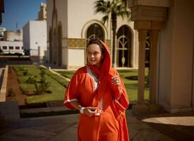 atraente meio Oriental muçulmano mulher dentro laranja tradicional roupas e lenço de cabeça, pensativamente olhando longe foto