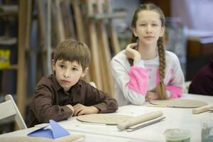 uma menina e uma Garoto estão sentado às uma escrivaninha dentro uma argila modelagem lição. foto