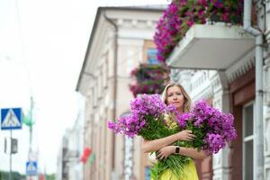 uma lindo idosos mulher com uma ramalhete do flores anda em por aí a cidade. era modelo loiro com azul olhos é feliz. uma mulher do cinquenta anos anda em dentro a verão, tendo uma Boa tempo. foto