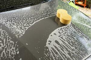 carro limpeza e lavando com amarelo esponja e espuma Sabonete foto