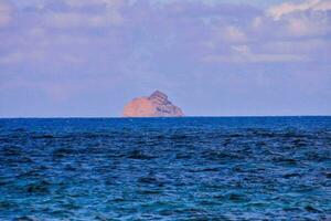 uma Rocha dentro a oceano com uma azul céu foto