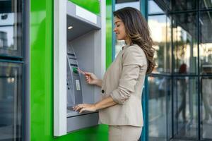 mulher retirada dinheiro às a atm. jovem mulher retirada dinheiro a partir de crédito cartão às atm foto