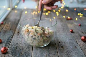 caseiro Novo ano é olivier salada em uma de madeira fundo. uma do homem mão coloca uma tradicional russo Natal salada com uma colher. foto