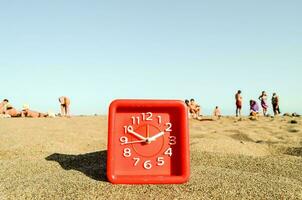 uma vermelho relógio em a de praia com pessoas dentro a fundo foto