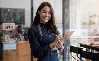retrato de um sorridente empresário asiático em pé atrás de seu café foto