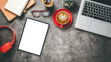 escritório escrivaninha local de trabalho com em branco tela tábua, computador portátil, fone de ouvido, caderno, óculos e copo do café, topo Visão plano deitar com cópia de espaço. foto