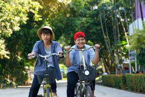 dois ásia Rapazes quem estão amigos passeio bicicletas dentro a local parque em feriado. elas estão ambos feliz e tendo Diversão. feriado atividade conceito. suave e seletivo foco. foto