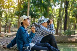 meninos asiáticos usam binóculos para observar pássaros em uma floresta comunitária própria. o conceito de aprendizagem a partir de fontes de aprendizagem fora da escola. foco no primeiro filho. foto