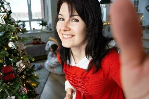 selfie retrato do uma mulher dentro uma vermelho santa vestir dentro uma casa interior com uma Natal árvore e Novo ano decoração. preparação para a feriados, festa foto