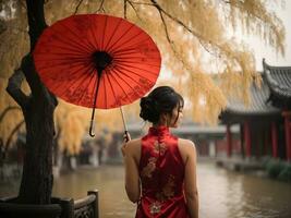 ásia mulher dentro vermelho vestir cheongsam segurando vermelho guarda-chuva perto salgueiro árvore. foto