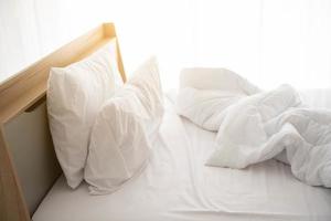 cama branca desarrumada pela manhã com sol foto
