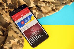 Kyiv, Ucrânia - 4 poderia, 2023 24tv ucraniano notícia portal em Smartphone tela com ucraniano bandeira e camuflar tecido foto