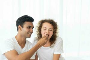 sorridente e feliz casal tendo sobremesa dentro cama dentro a manhã foto