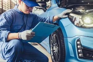 Técnico de mecânico de automóveis asiático segurando a prancheta, verificando a manutenção