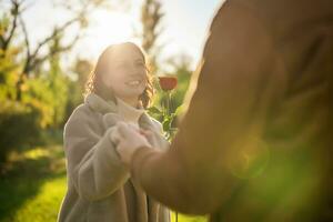 retrato do feliz amoroso casal dentro parque dentro pôr do sol. homem é dando rosa para dele mulher. foto