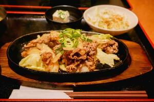 japonês Comida quente panela frito carne de porco com japonês molho e salada em Preto bandeja fundo. foto