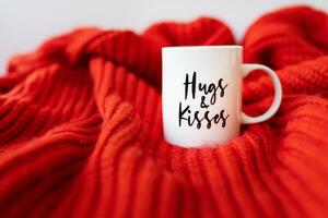uma branco copo com uma coração carrinhos em uma vermelho tricotado tecido. inscrição do st. dia dos namorados dia, 14 fevereiro. foto