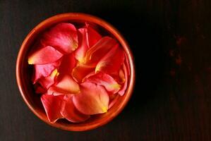 rosa pétalas dentro uma tigela em uma Sombrio de madeira fundo. foto