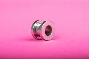 piercing, túnel de ouvido prateado em close-up de fundo rosa foto