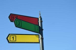 uma pilar com colori direção Setas; flechas e destino números contra a céu. metal rua placa. Lugar, colocar para nomes. foto