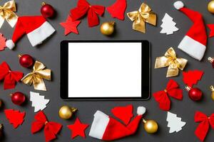 vista superior do tablet digital em fundo preto com brinquedos e decorações de ano novo. conceito de tempo de natal foto