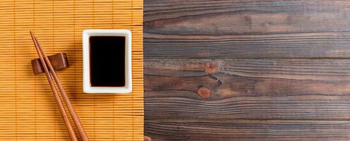 esteira de bambu e molho de soja com pauzinhos de sushi na mesa de madeira. vista superior com fundo de espaço de cópia para sushi. postura plana foto