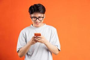 jovem asiático alegre usando telefone isolado em fundo laranja