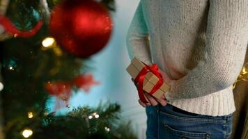 a cara detém uma Novo anos presente atrás dele voltar. traseiro Visão do uma homem segurando uma presente caixa atrás dele costas contra a pano de fundo do uma Natal árvore. foto