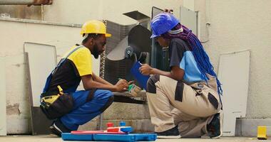 africano americano trabalhadores varrendo longe solto detritos acumulado por aí condensador base. especialista engenheiros limpeza hvac sistema corpo e ao controle painel com varredura escova ferramenta para retirar solto sujeira foto